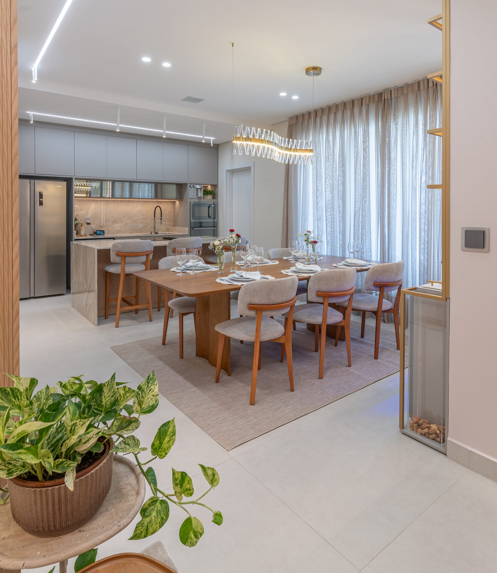Sala de jantar integrada à cozinha, com mesa em madeira e pendente de cristal