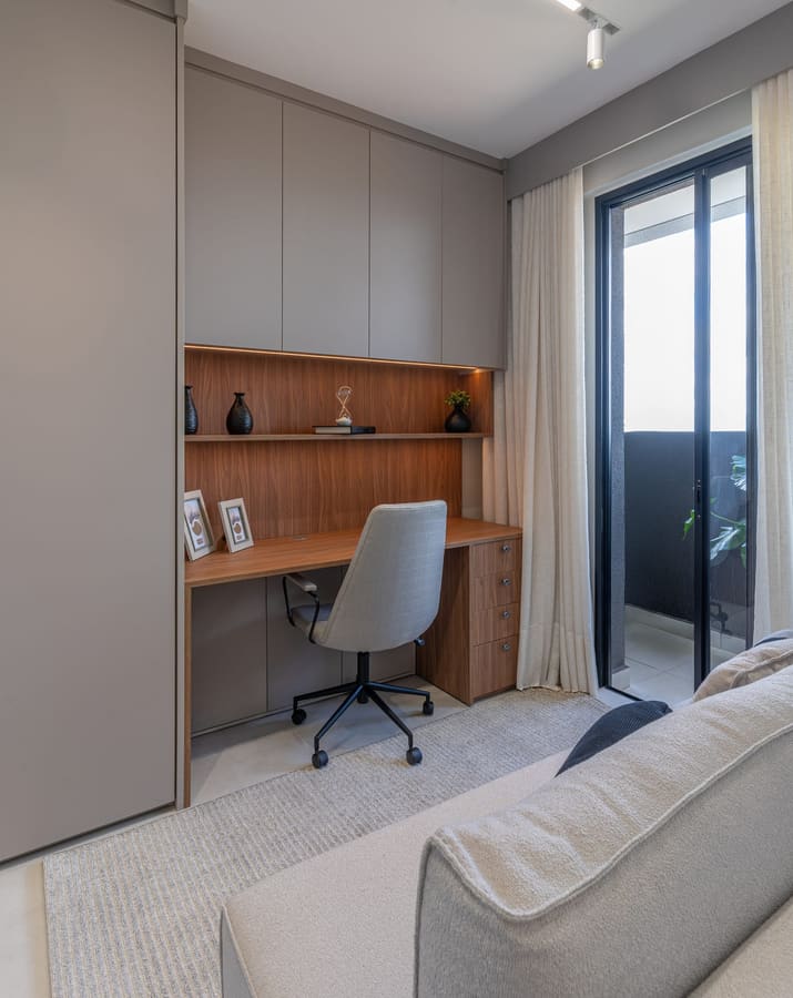 Home office com bancada em madeira, sofá e porta de vidro para a varanda
