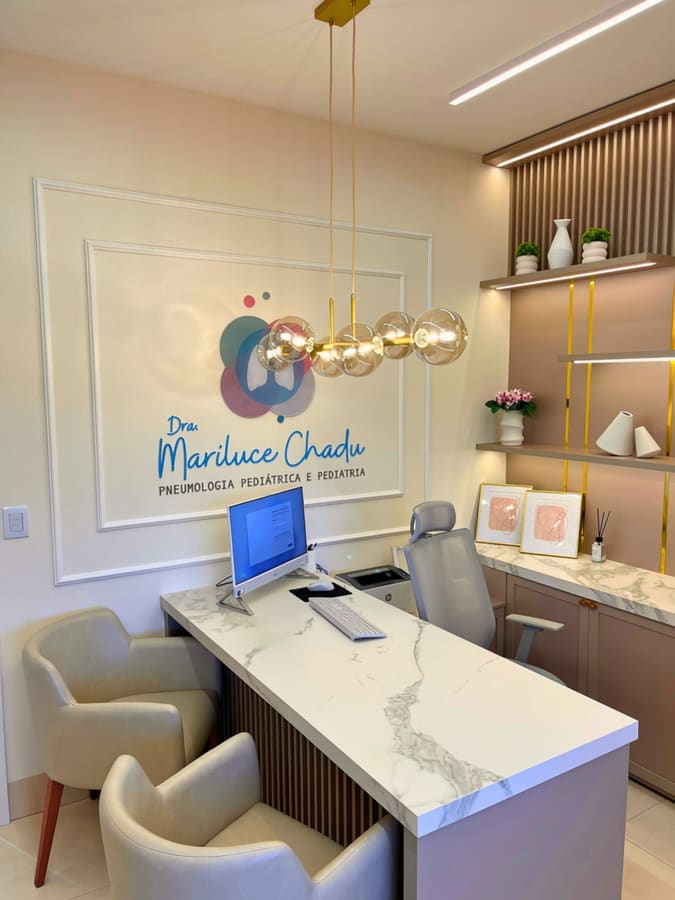 Mesa de atendimento em pedra branca com poltronas e logotipo da médica na parede