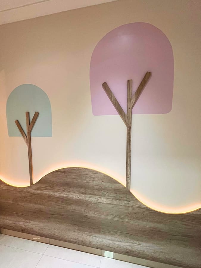 Parede com árvores ilustradas e onda em madeira com iluminação embutida