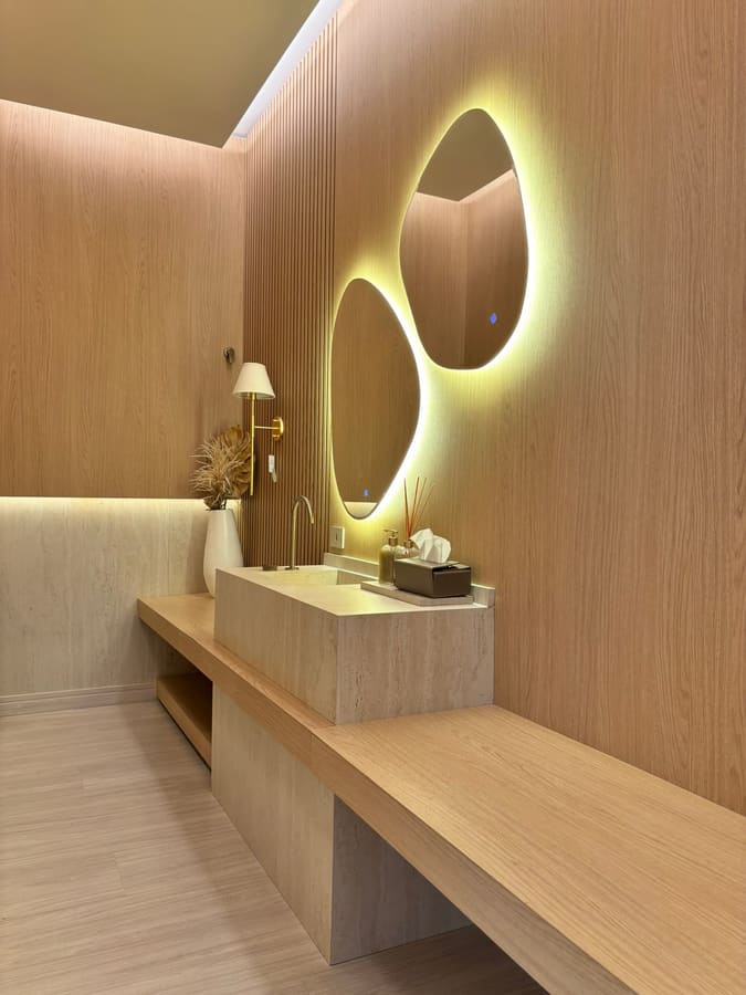 Lavabo com espelhos orgânicos retroiluminados e revestimento em madeira