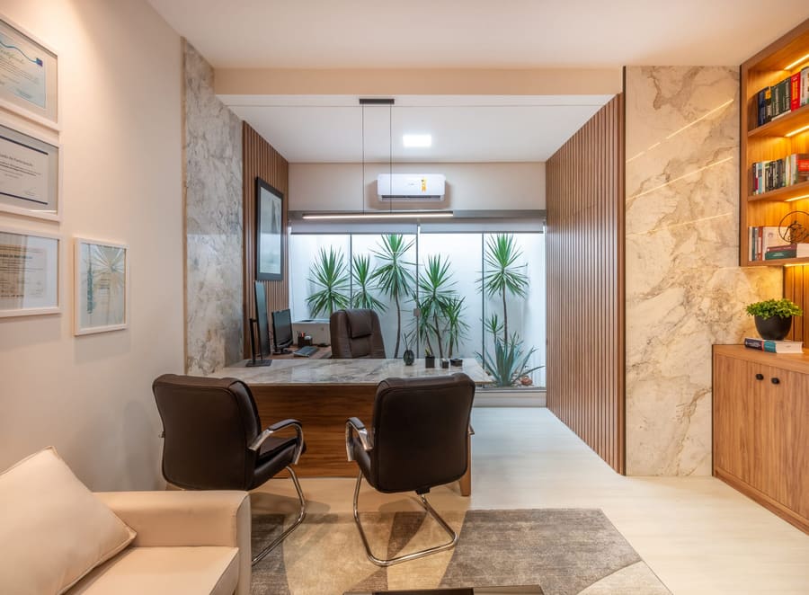 Sala do advogado com mesa executiva, revestimento marmorizado e jardim ao fundo