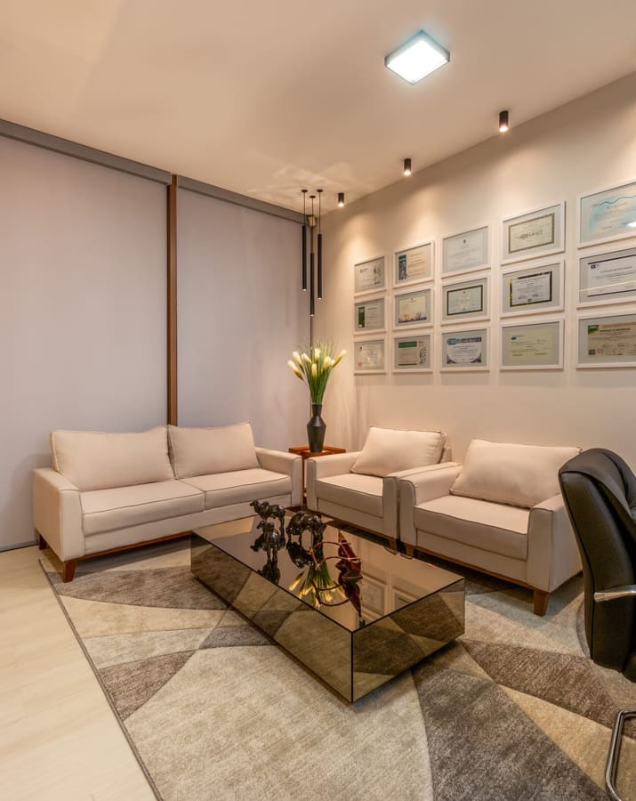 Sala de espera com sofás claros, mesa de centro espelhada e quadros na parede